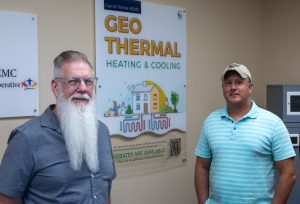 Two men standing in front of a geothermal program sign.